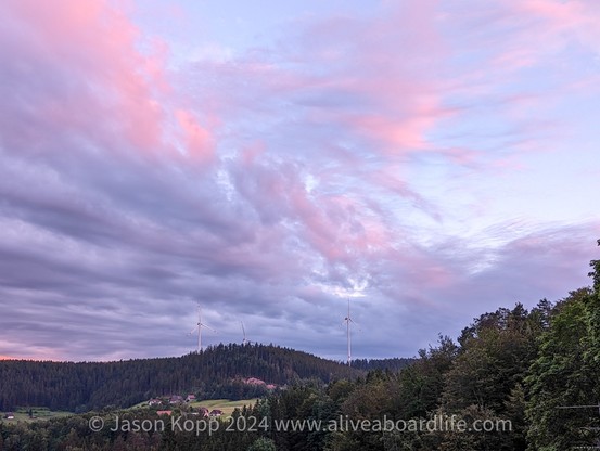 Pink and purple clouds over same hill with forest and windmills