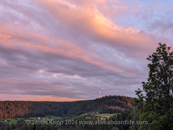 Pink and gold clouds in bands over hill with forest and windmill