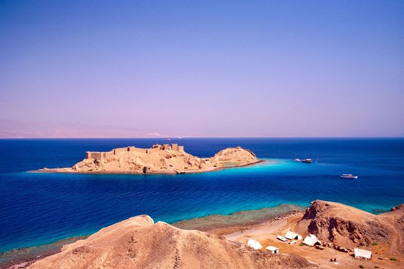 Small rocky island just off the coast of Sinai Peninsula in Egypt. On the summit a ruins wall from the middle ages time. Rocks are ochre, while the sea, the Red Sea, is deep blue with turquoise nuances. 