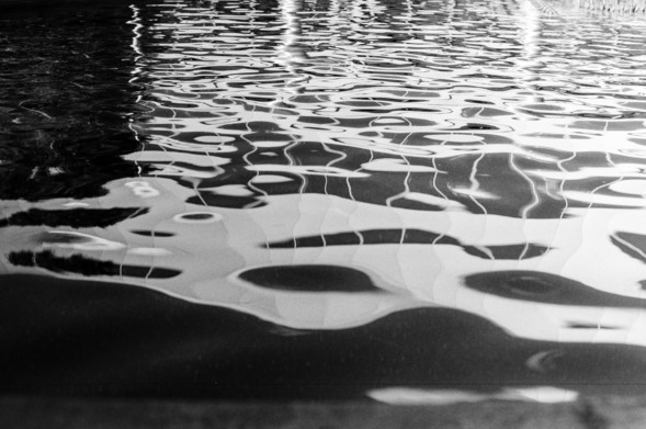 Rippling water in a fountain, reflecting a building and sunlight off the surface