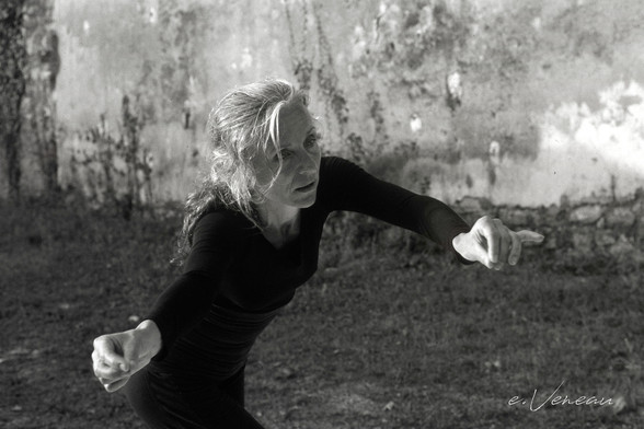 In the foreground a woman dances dressed in black in a blurred setting which appears to be a wasteland.