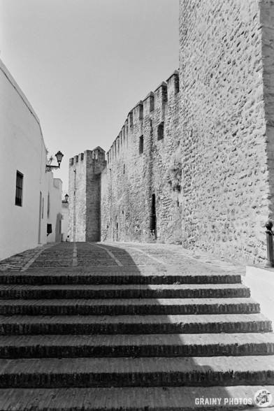A black-and-white film photo of a cobbled passage around the old town walls.