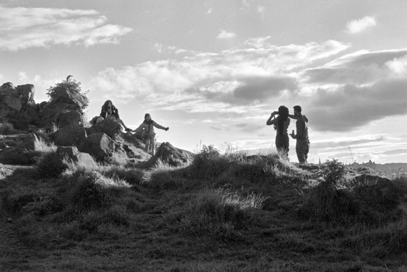 Two people stand silhouetted, taking a photo of two other people silhouetted, slightly higher up the hill in this black and white photo.