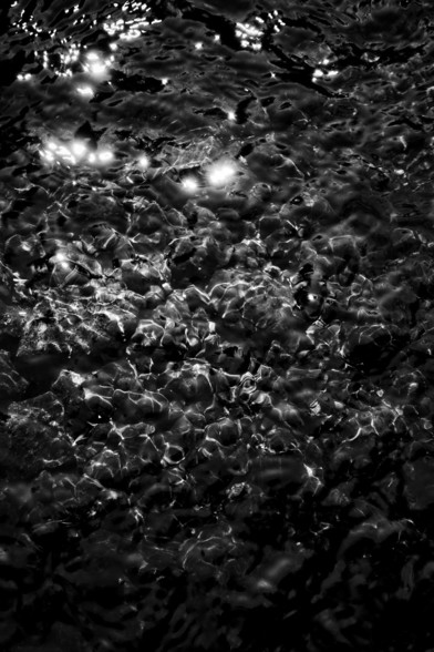 Light falls on shallow water in a stream, highlighting the shapes and textures of the small pebbles on the bed