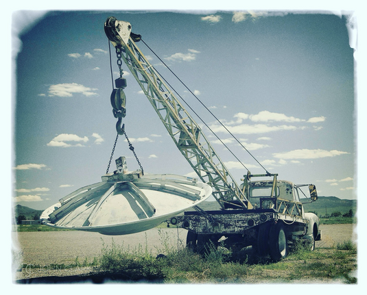 An old tow truck with a “UFO” hanging from the hook in the back