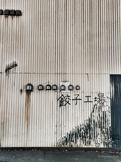 The rusted wall with black door on the corner and hand written “Dumplings Factory “ sign