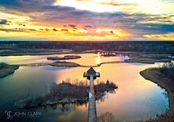 Drone view of the wet marshland with a boardwalk. Vivid sunset in the clouds and reflecting off the water. 