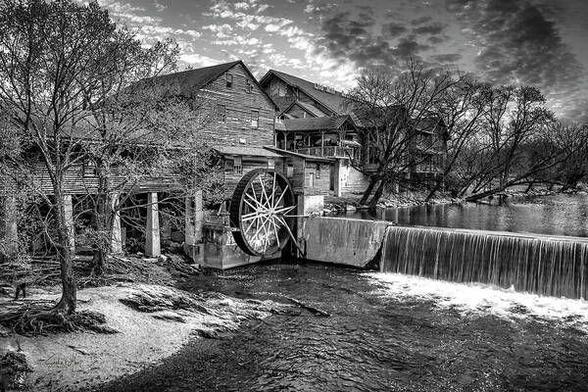 Black and white photo of The Old Mill in Pigeon Forge, Tennessee, showing the mill's rustic structure and waterwheel beside a calm river in the Great Smoky Mountains.  From the Fine Art Gallery of Shelia Hunt.