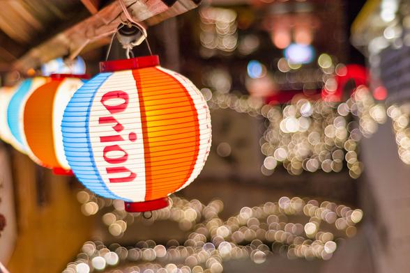 Colorful paper lanterns with the word "Orion" are hung, creating a festive atmosphere. A blurred background of warm lights adds to the ambiance.