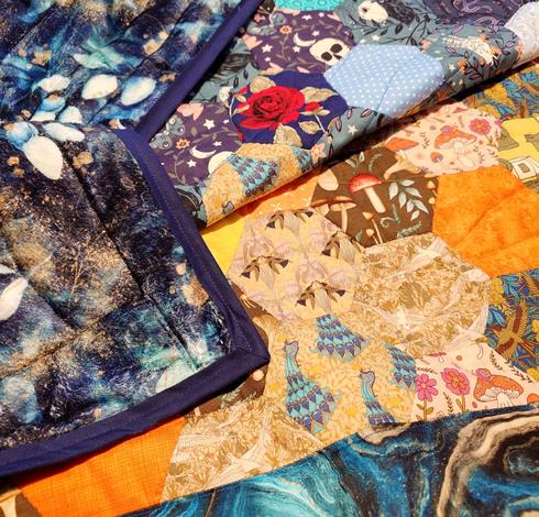 A closeup of the different patterns and colours that make up the aforementioned quilt, including the fleece backing which is dark teal with golden leaves on it. 
