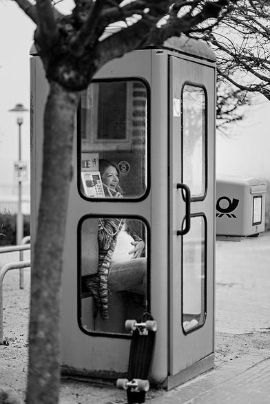 Schwangere Frau sitzt in einer Telefonzelle und telefoniert.