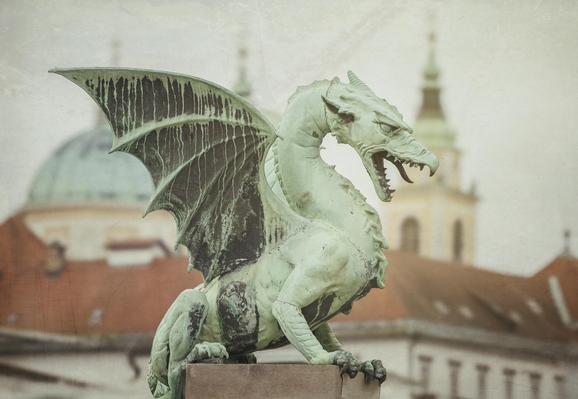 A statue of a dragon sits atop a concrete pillar on the Dragon Bridge in Ljubljana Slovenia. In the softly blurred background are spires and domes of the city's churches. There are texture overlays on the photo. 

https://joan-carroll.pixels.com/featured/dragon-bridge-statue-2-ljubljana-slovenia-joan-carroll.html

#dragon #statue #ljubljana #slovenia #wings #sculpture #monument #mythical #travel #travelphotography #textures #spires #domes #AYearForArt #buyIntoArt #giftideas #wallart #artforsale @joancarroll