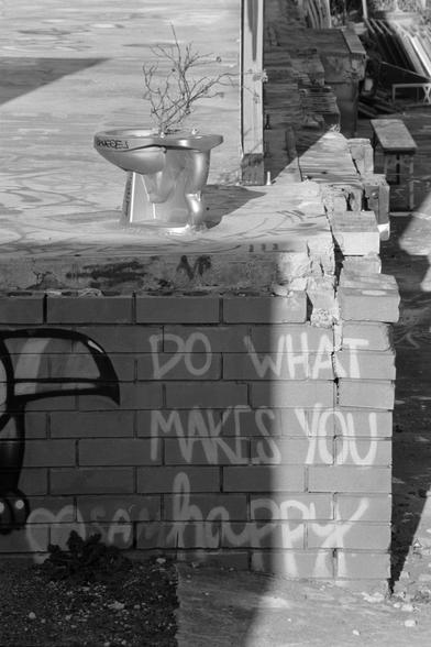 A shiny painted toilet on the slab of an old warehouse, with “do what makes you happy” in graffiti underneath