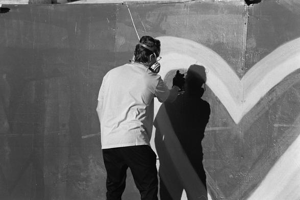 A person with a respirator on spraying a giant heart in graffiti