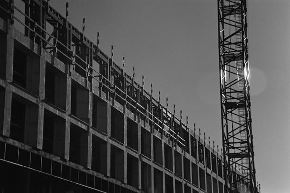 An apartment building under construction, the last bit of sun painting it from the side and lighting up part of the crane