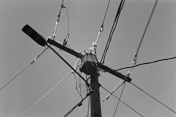 A power pole from below, with a transformer and streetlight, ceramic insulators shining in the sunlight 