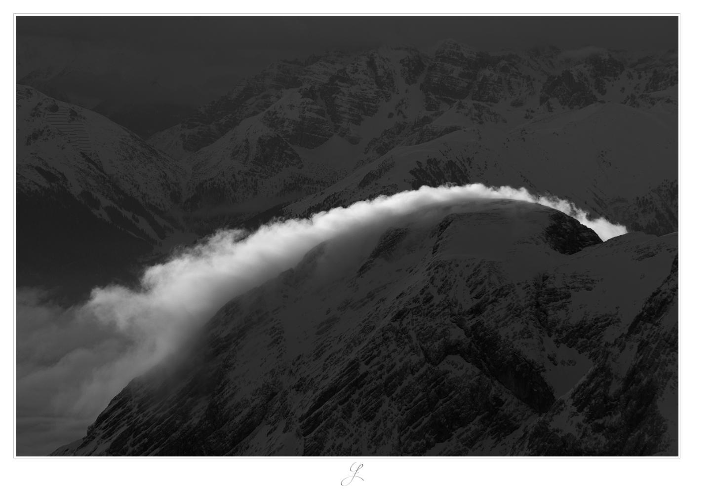 Inbetween
A landscape shot of a mountain peak with a chain of summits in the background. Along the slope of the peak in the foreground, thin white clouds drift over the mountain top. The clouds are brightened by the sun, the rest is much darker. This is a high contrast image in black and white.

AI disclaimer: Using my work, its meta data, written or derived description to create media with or train AI based systems is prohibited.