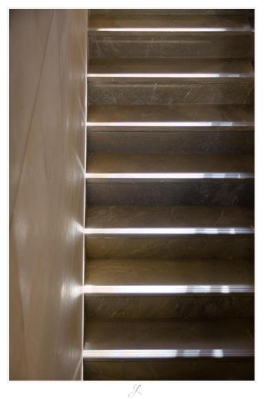 View from above of marble steps of a staircase leading along a stone wall. The sunlight from the top right shines on the steps. The next step up casts its shadow on the step below. This creates a strip of light on the front edge of each step and from there a line-like reflection on the stone wall. The colors are warm, ocher tones.

AI disclaimer: Using my work, its meta data, written or derived description to create media with or train AI based systems is prohibited.