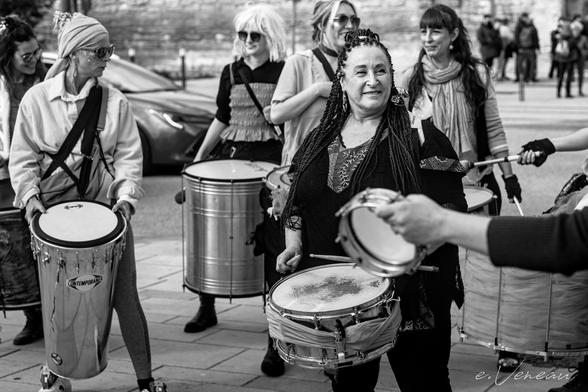 Smiling women carrying various percussion instruments prepare to demonstrate.