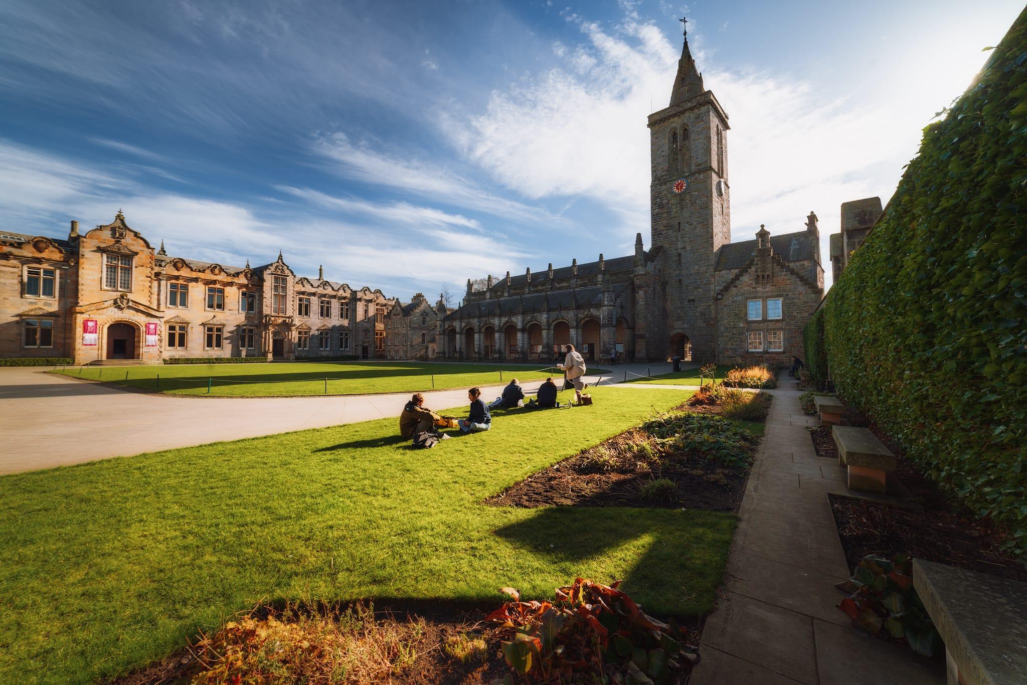 St Salvator's Quadrangle at the University of St Andrews, featuring a picturesque scene with historic stone buildings and a tall clock tower. The quadrangle is filled with lush green grass, where a group of people are seated, enjoying the outdoors. The buildings display intricate architectural details, including large windows and decorative elements, with some areas adorned with pink banners. In the foreground, a neatly paved path leads through the well-maintained gardens, lined with flower beds. Above, the sky is bright with scattered clouds, enhancing the inviting atmosphere of the university setting.
St Salvator's Quadrangle at the University of St Andrews, featuring a picturesque scene with historic stone buildings and a tall clock tower. The quadrangle is filled with lush green grass, where a group of people are seated, enjoying the outdoors. The buildings display intricate architectural details, including large windows and decorative elements, with some areas adorned with pink banners. In the foreground, a neatly paved path leads through the well-maintained gardens, lined with flower beds. Above, the sky is bright with scattered clouds, enhancing the inviting atmosphere of the university setting.