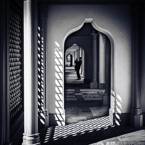 Schwarz und Weiss-Bild in einem Gang der (Schau-)Moschee des Schlossparks Schwetzingen. In einiger Entfernung ist die gekrümmte Silhouette eines Mannes zu sehen. Er fotografiert mit einem Handy schräg nach oben.