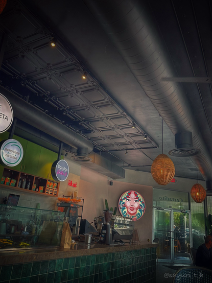Cafe counter decorated with green tiles and green background wall. Ceiling is black with metal duct and vent