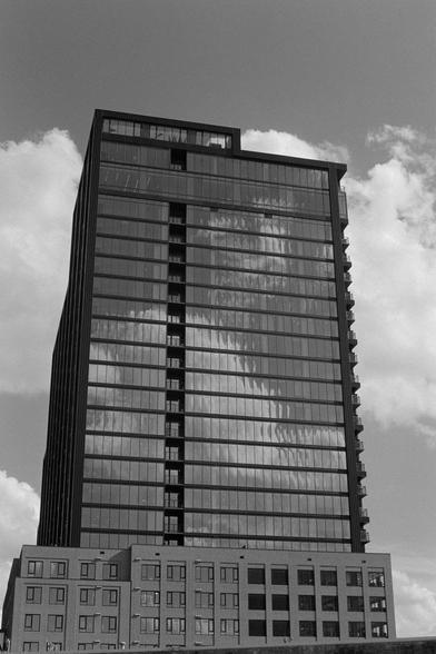 A glassy building with cloudy sky behind and a reflection of more cloudy sky on the front