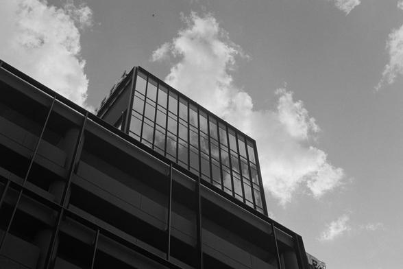 Looking up a glassy building with a partially cloudy sky, with more clouds reflected in the building’s exterior