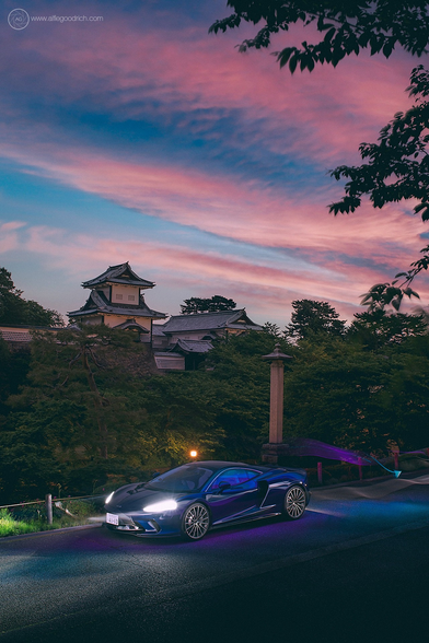 A McLaren GT supercar in front of Kanazawa Castle at dusk. The car's lights are on. We also did some light painting around the car in various colours complimentary to the scene. The sky is vivid with the last light of the day. 
