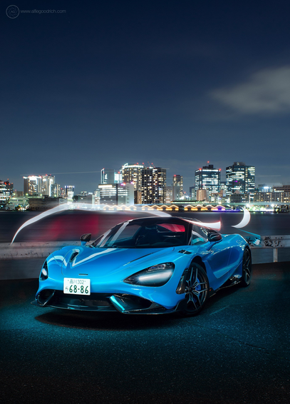 A light blue McLaren 765LT supercar parked on the quayside in Tokyo, one very cold December night a few years back. The end of a long day of shooting this 765LT and a 750S around various locations in Tokyo. In the background we see a chunk of the illuminated nighttime cityscape of high rise buildings. The sky is almost cloudless. I've light painted around the car in this 90second exposure. 