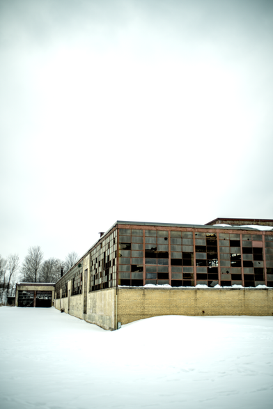 Abandoned industrial building in snow – A large, derelict brick and steel factory stands empty in a snow-covered field under an overcast sky.