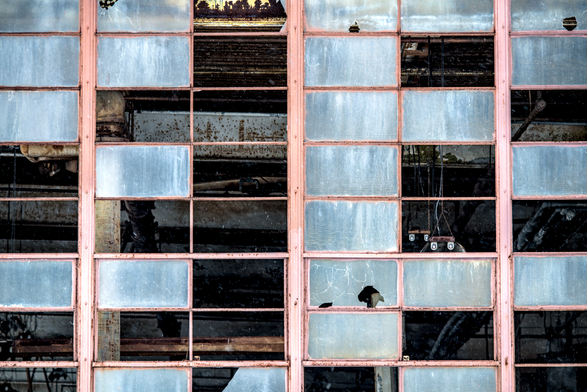 Close-up of broken industrial windows – A section of tall, rust-framed windows with many cracked and missing panes reveals a dark, decaying interior.