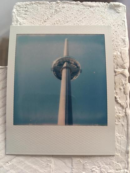 Polaroid photo: The i360 tower and the shiny doughnut shaped lift rise into the clear blue sky.