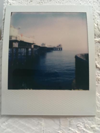 Polaroid photo: a blurry look towards the end of the Brighton Palace pier out to sea with the red and white tower of the heater skelter and other funfair rides visible on the edge of the pier.