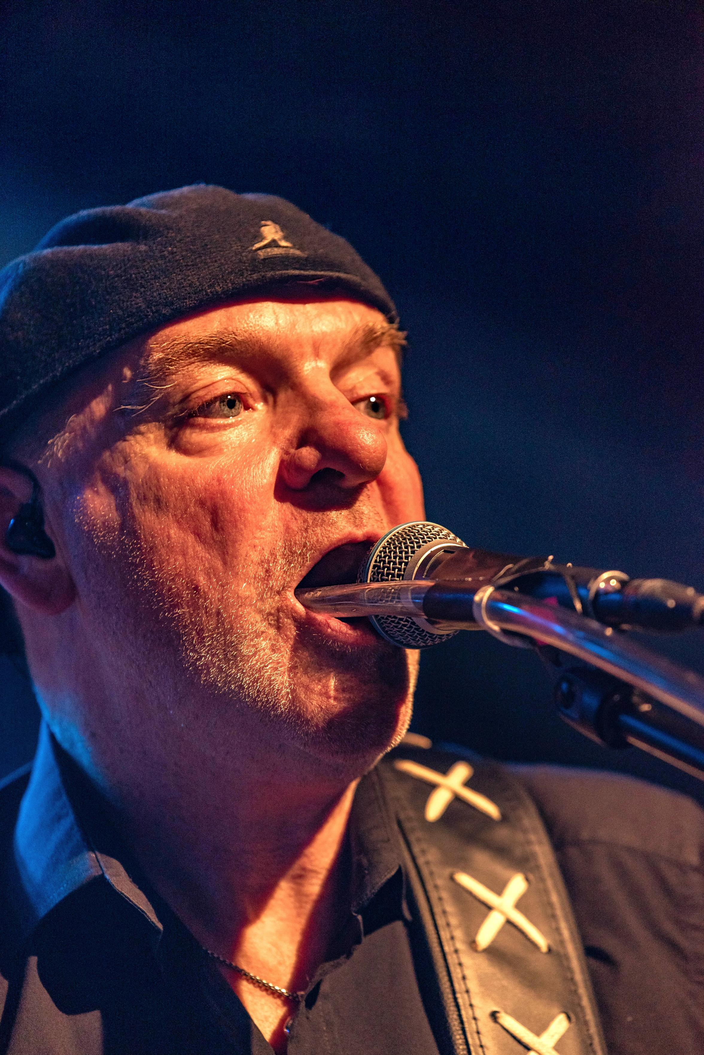 Ein Sänger steht mit offenem Mund vor seinem Mikrofon und ein durchsichtiger Schlauch geht bis in seine Mundhöhle.