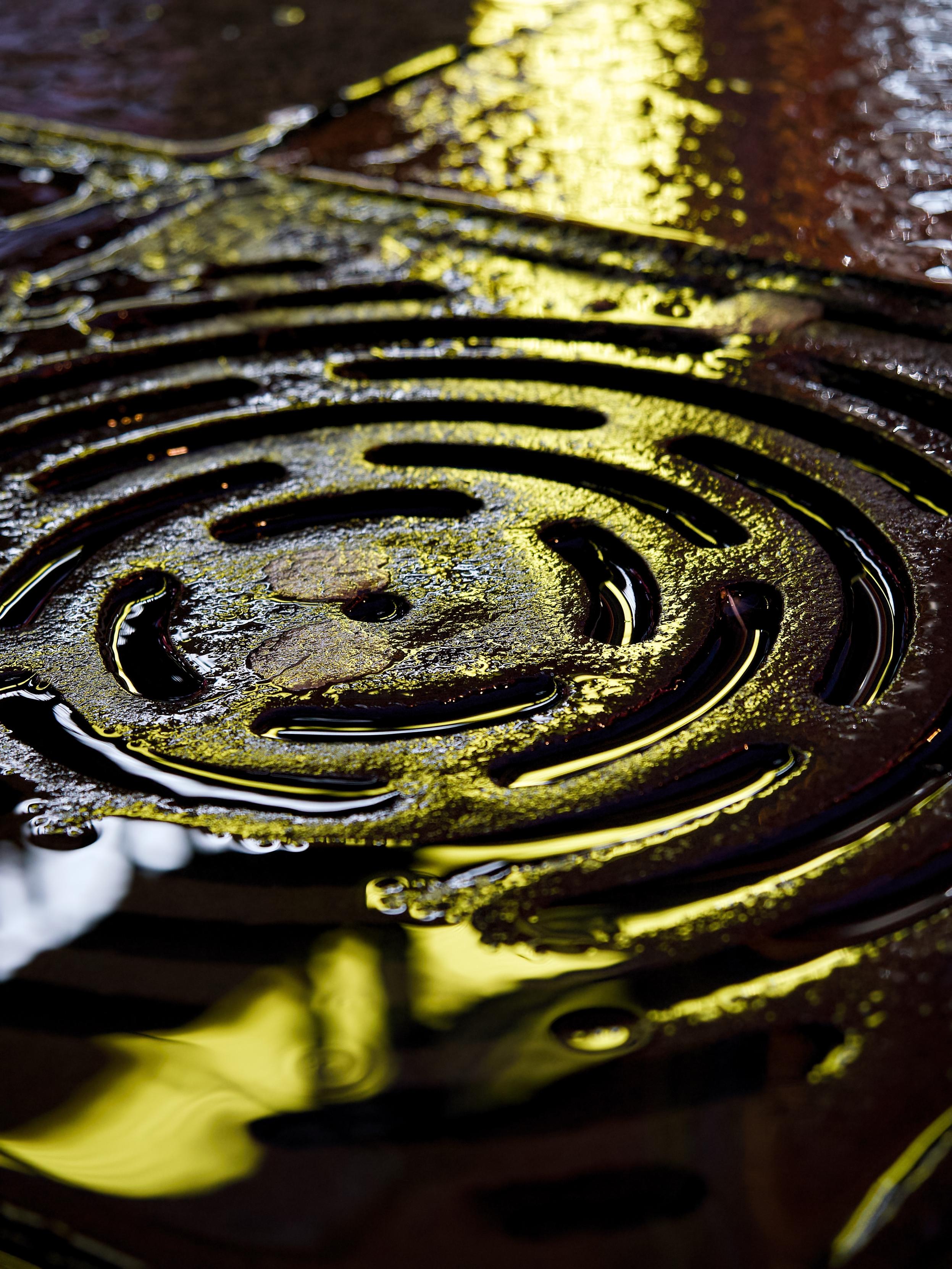 Golden light reflects on the rainwater around a circular iron street drain, making it look like it has been cast from precious metal