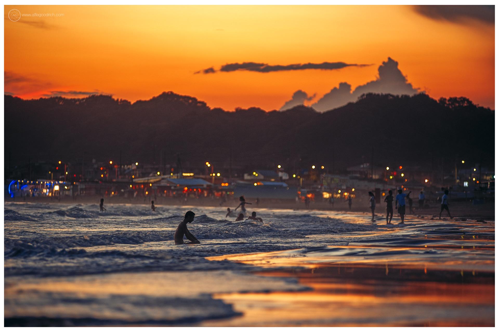 North beach, Kamakura, back in the summer of 2012. Surfers are in the waves. Lights on the coast road behind. North beach, Kamakura, back in the summer of 2012. Surfers are in the waves. Lights on the coast road behind.