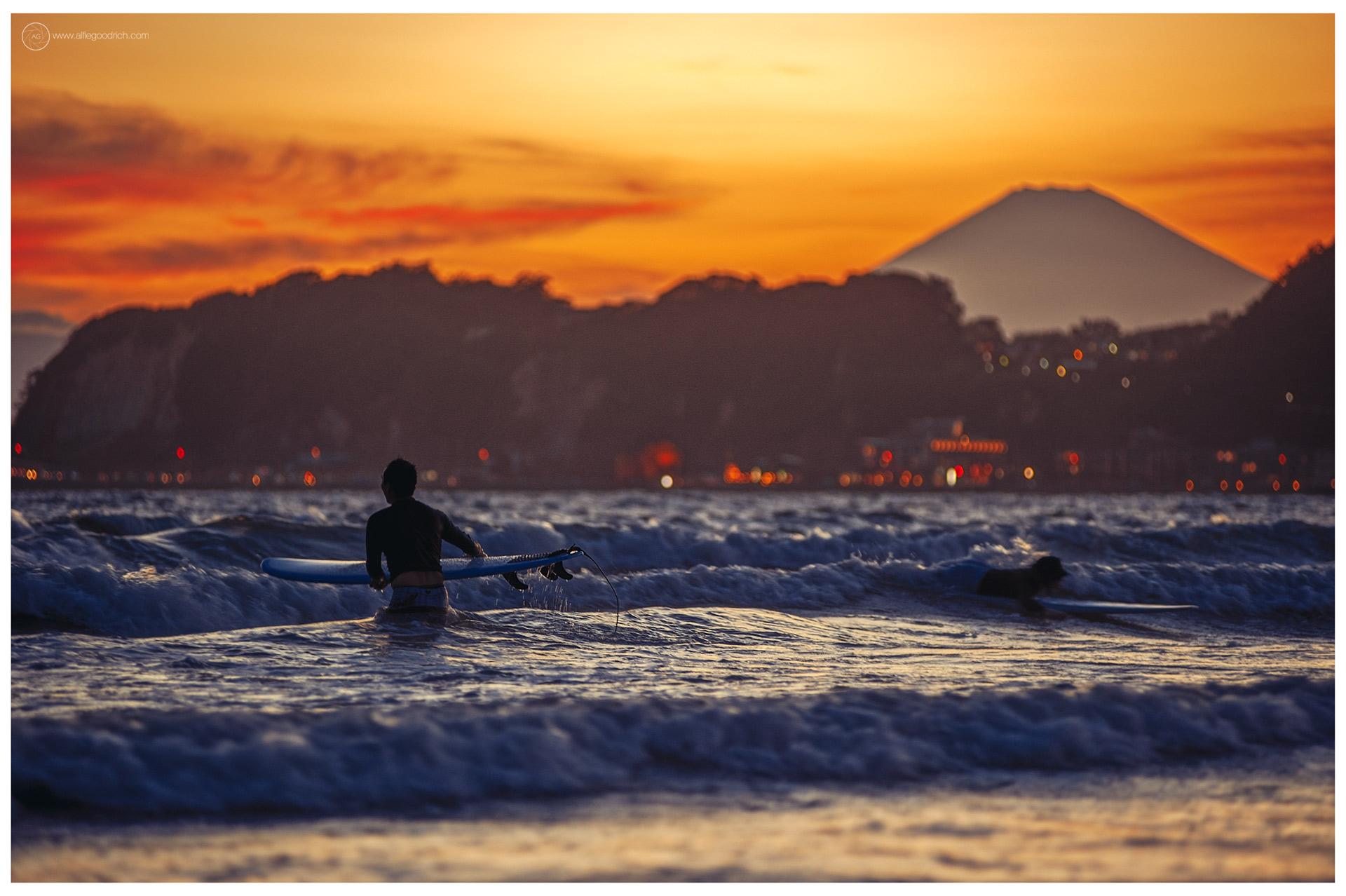 Mount Fuji at sunset, shot from north beach Kamakura back in the summer of 2012. Surfers are in the waves. Lights on the coast road behind. Fuji-san poking above the hills. Mount Fuji at sunset, shot from north beach Kamakura back in the summer of 2012. Surfers are in the waves. Lights on the coast road behind. Fuji-san poking above the hills.