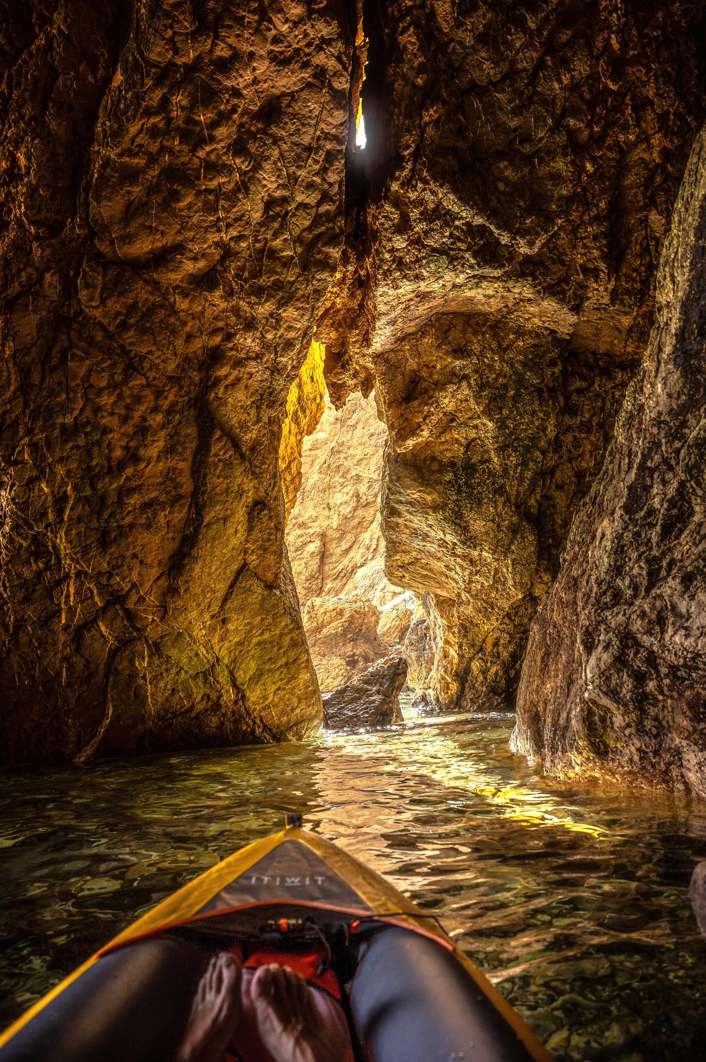 Der Bug eines aufblasbaren Kajak auf dem Wasser in einer Felshöhle. An einer Stelle der Felswand dringt Sonnenlicht durch einen Spalt. Der Bug eines aufblasbaren Kajak auf dem Wasser in einer Felshöhle. An einer Stelle der Felswand dringt Sonnenlicht durch einen Spalt.