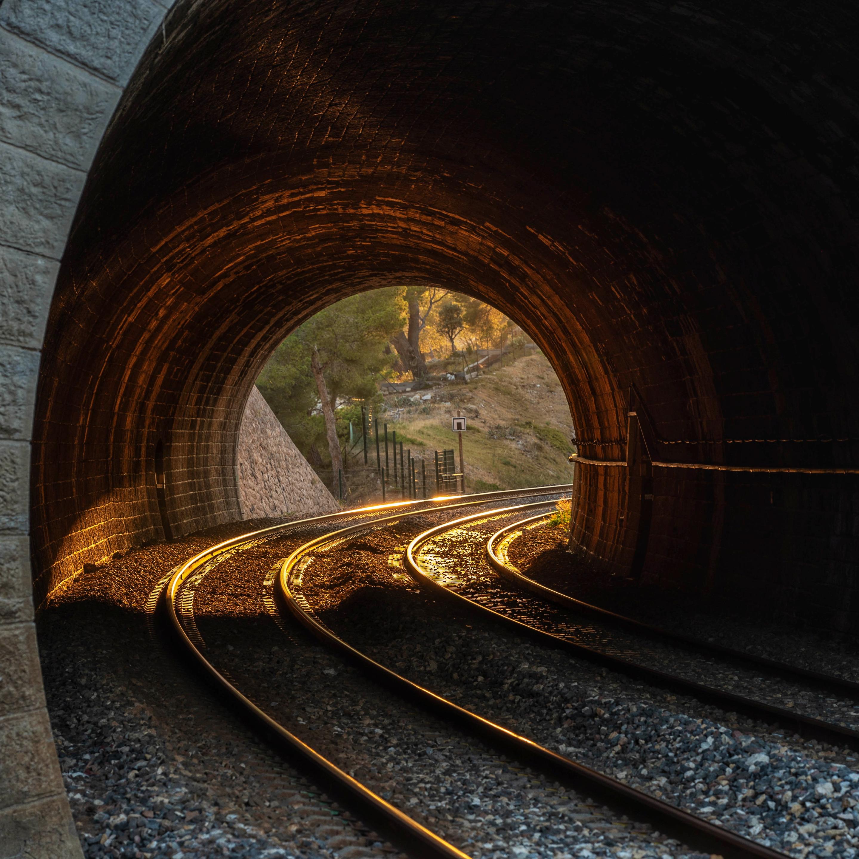Kurvige Bahngleise in einem kurzen Tunnel. Auf einer Seite scheint Sonnenlicht in den Tunnel. 