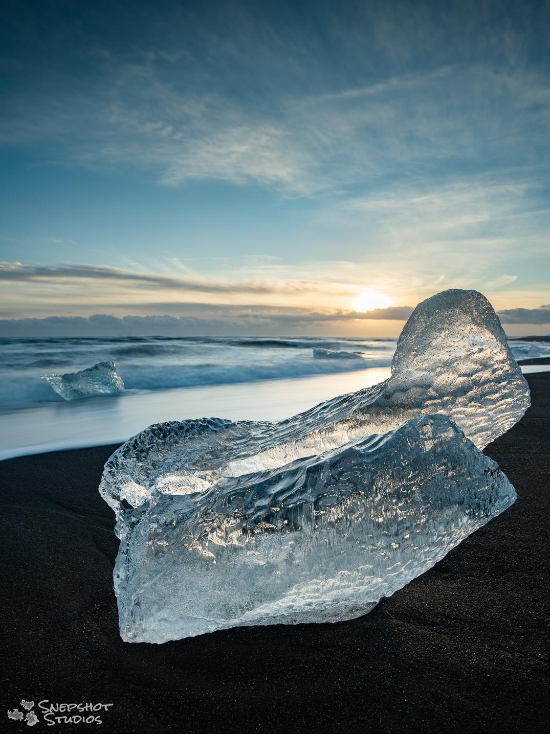 Iceland, Diamond Beach, a piece of clear glacier ice on a black sand beach with the sun setting behind it Iceland, Diamond Beach, a piece of clear glacier ice on a black sand beach with the sun setting behind it