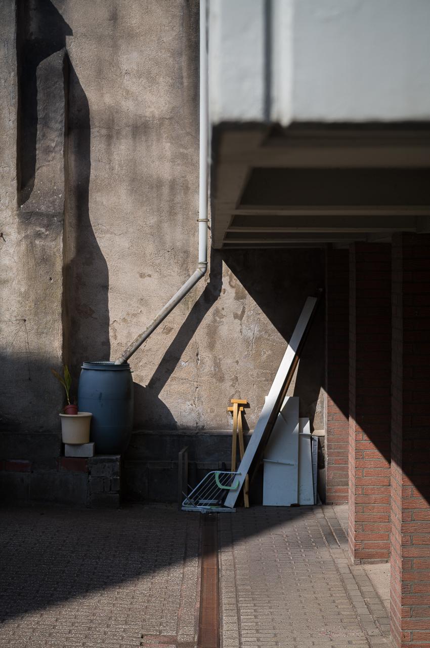 slanted shadows in a backyard - a drainpipe leading into a plastic barrel.