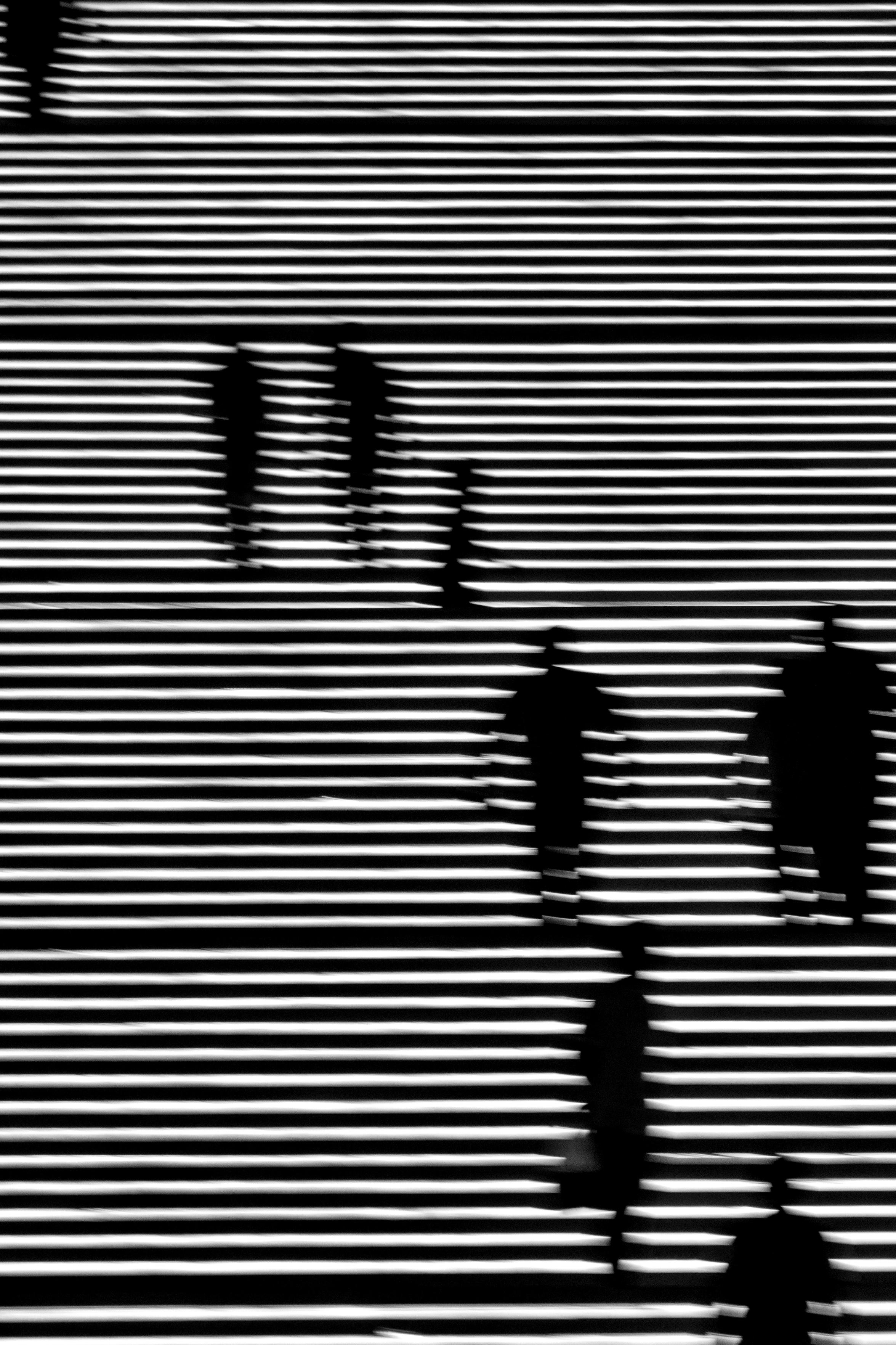 Black and white photo of an illuminated staircase. The image features a pattern of horizontal light strips representing the steps, with dark silhouettes of people visible climbing the stairs
