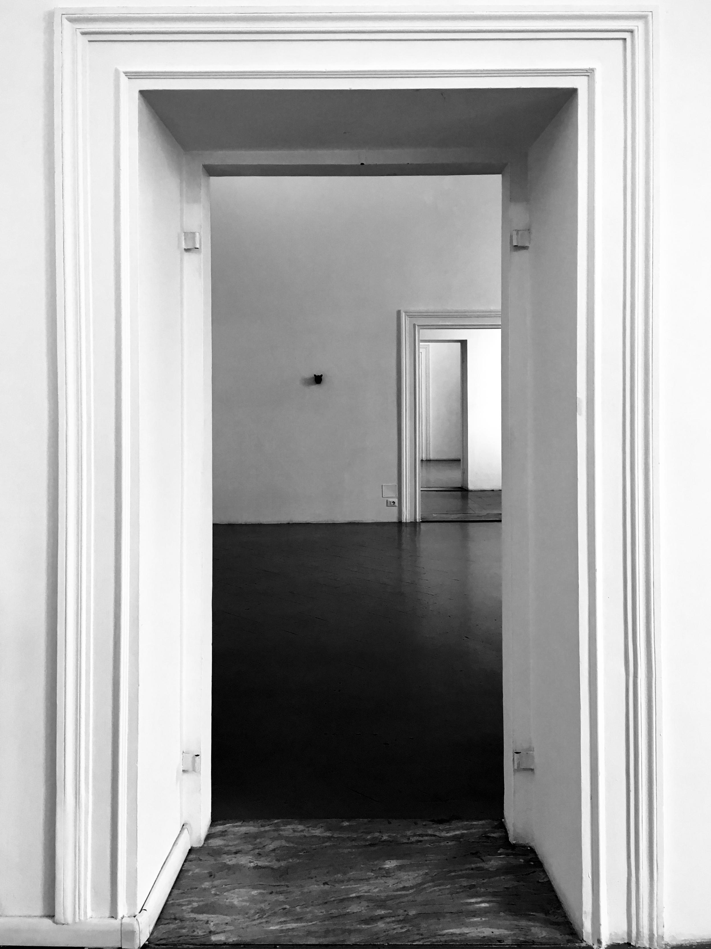 Black and white photo of a series of aligned doorways creating a tunnel effect. The view looks through three consecutive white door frames into empty rooms.
