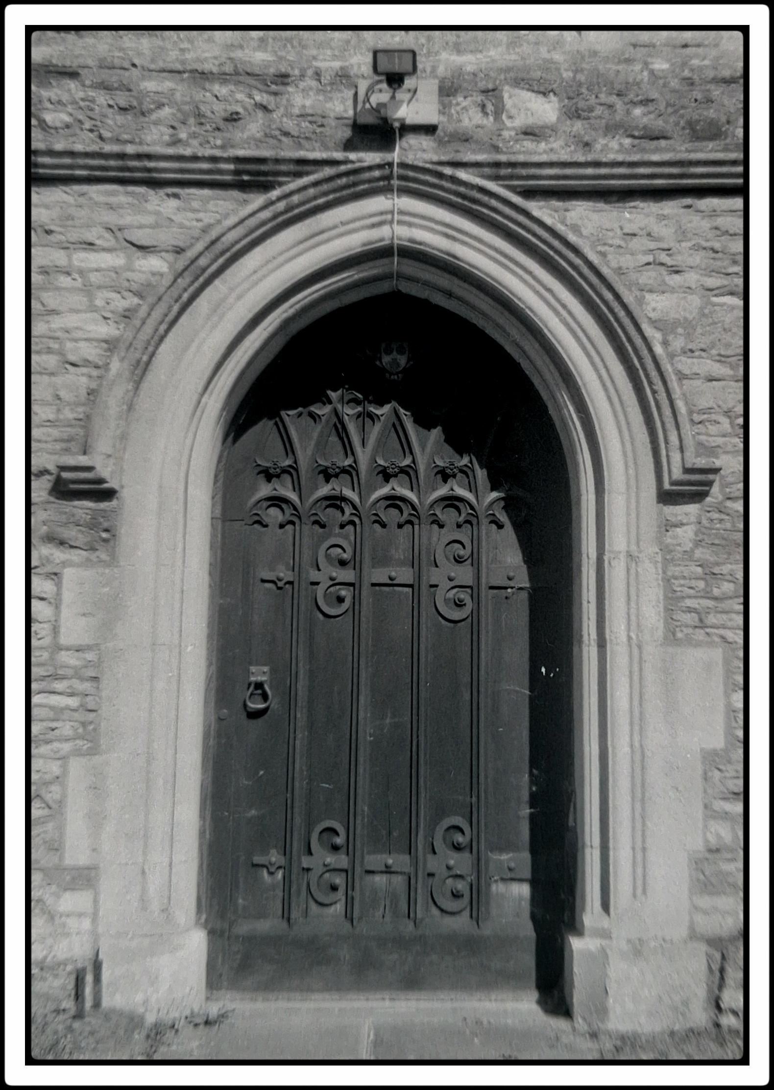 A grainy, black and white analogue image of a church door. Blurred edges