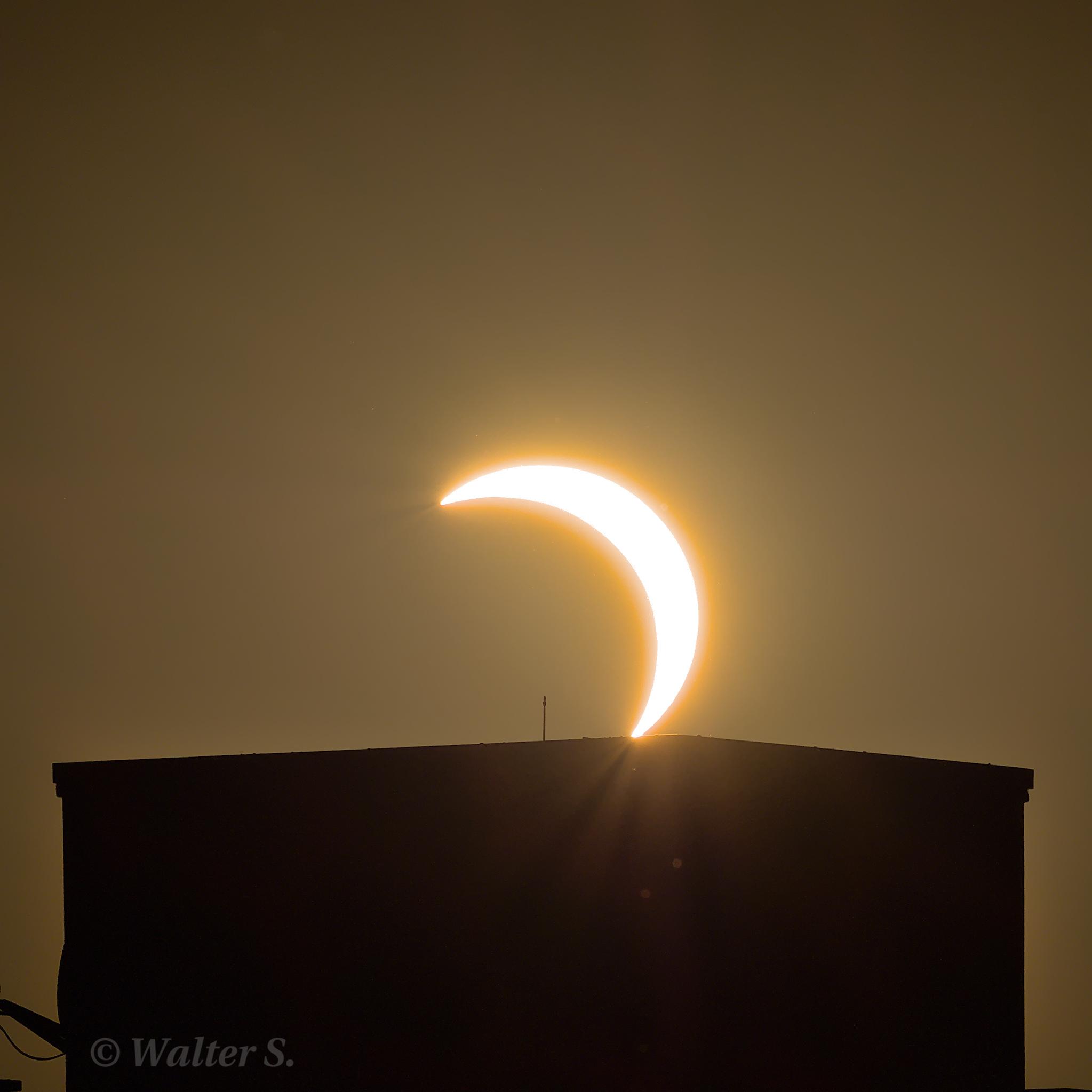 Partial solar eclipse with the sun just touching a flat roof