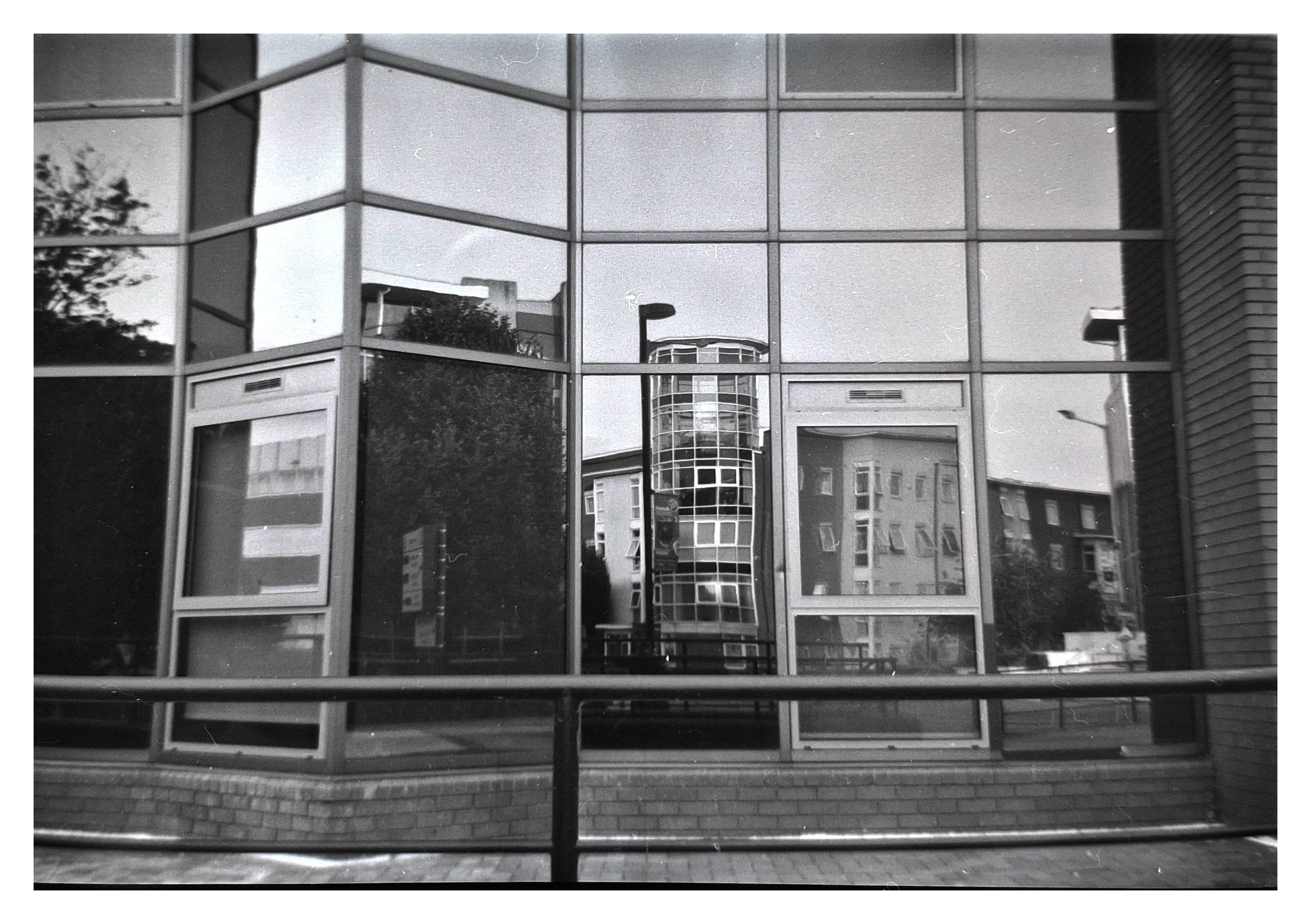 A black and white grainy image of buildings reflected in some office windows.