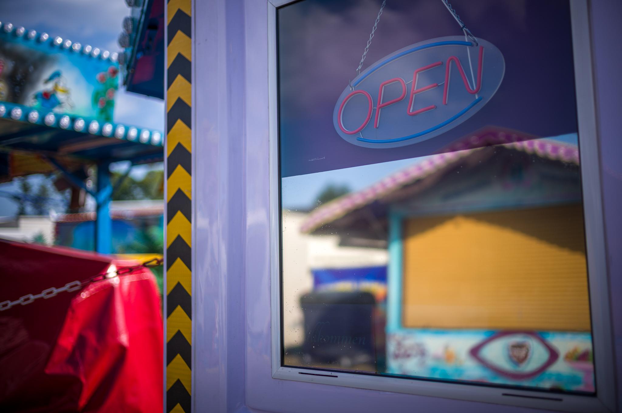 Closed box office on a fun fair with an "open"-sign, window reflecting opposite booth (also closed).