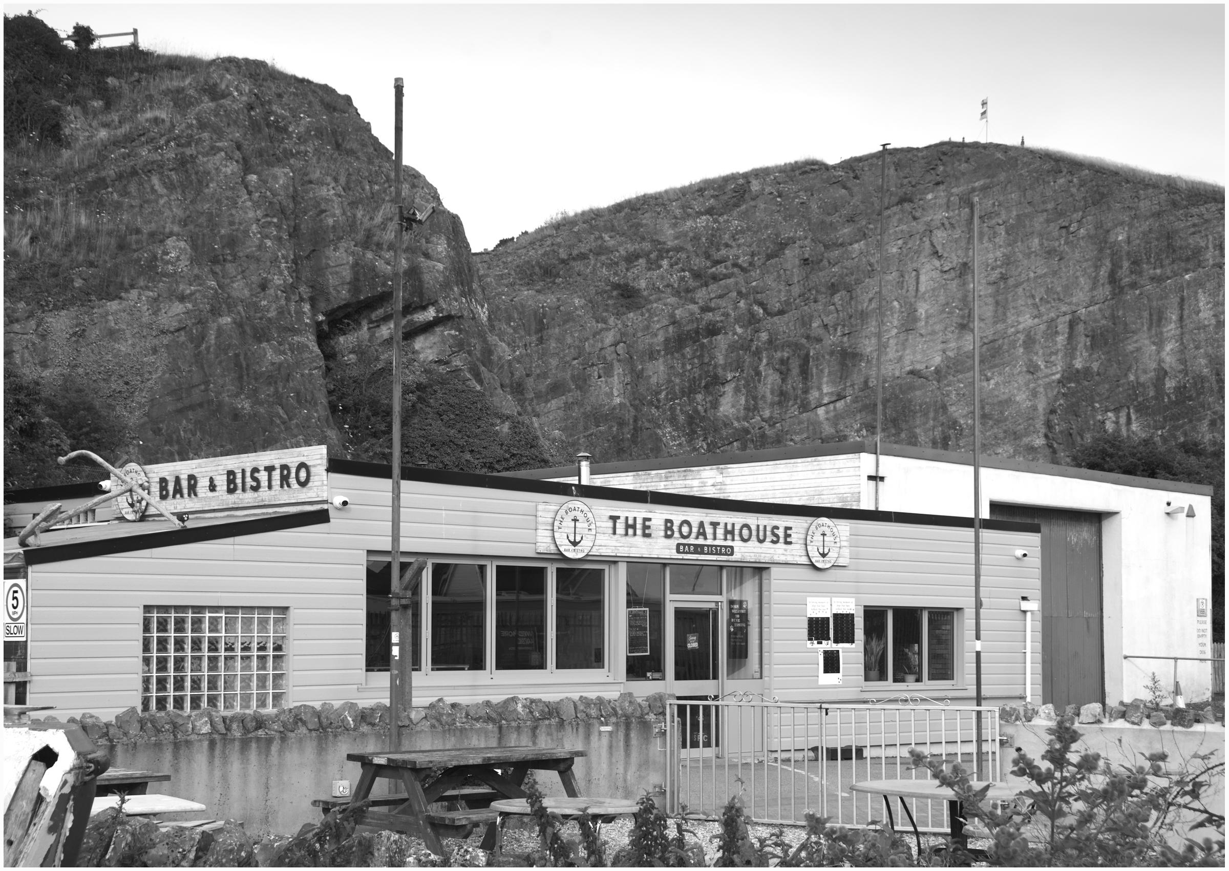 An evening black and white photograph taken at Uphill Boatyard, Weston-super-Mare, Bristol UK.
The image is of a Workshop Shed type building, constructed at the foot of a small cliff face. The Bar & Bistro are closed for business.