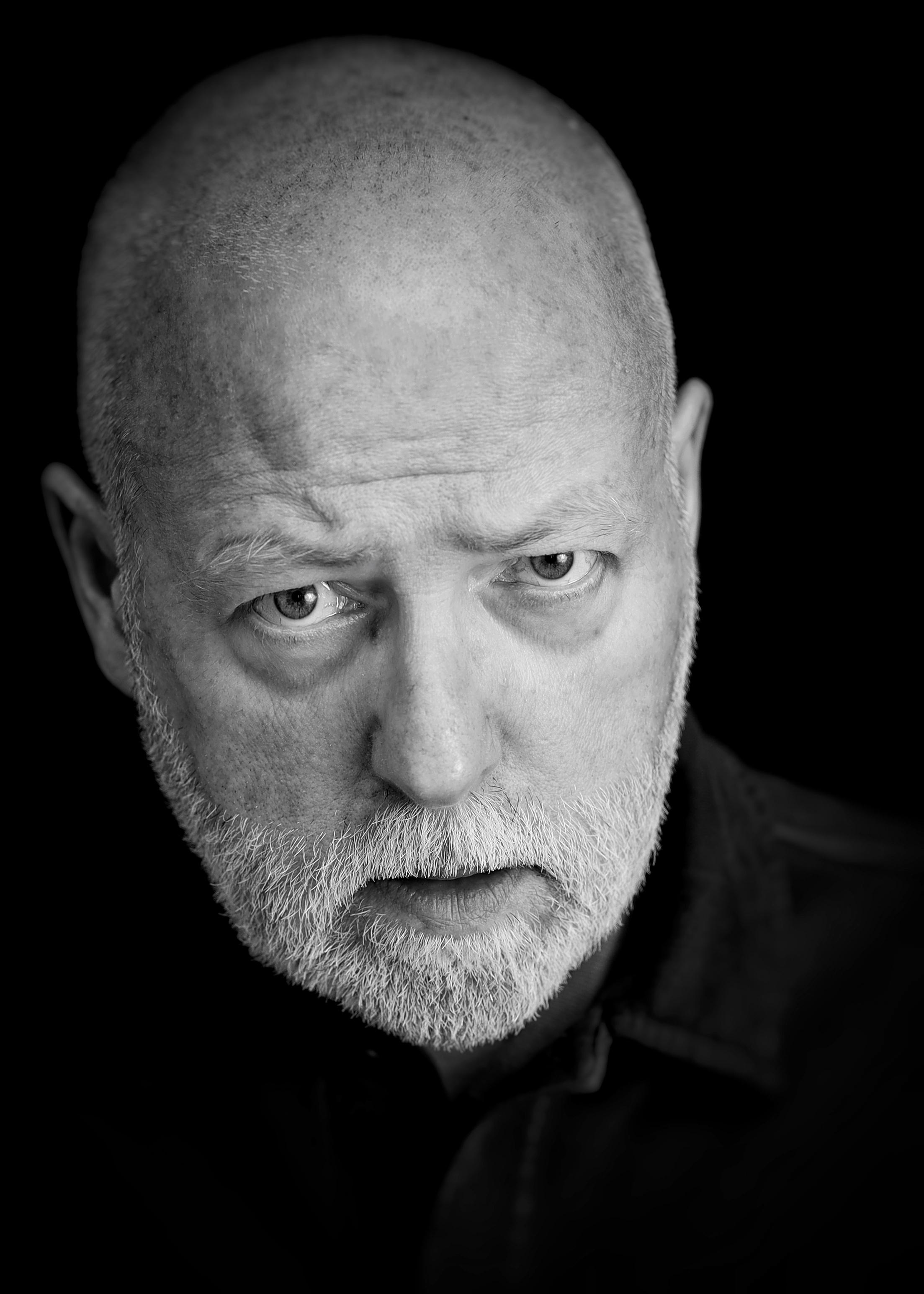 Male headshot. Bald with grey beard. Looking angry. Black and white.
